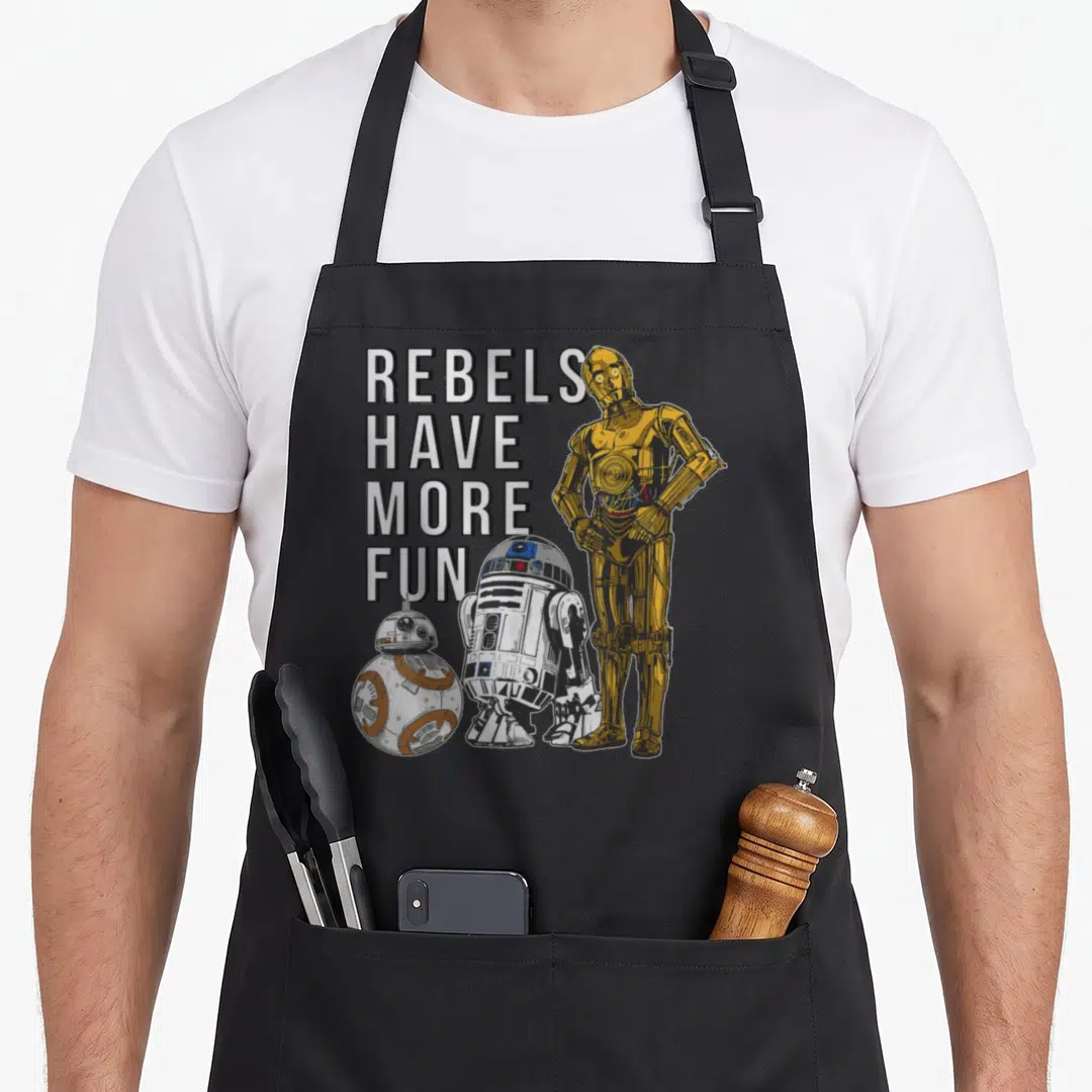 Droid droewors apron - C-3PO R2-D2 BB-8 robots with stacked text REBELS HAVE MORE FUN in gold and white — shown on a black cotton canvas apron against a white background