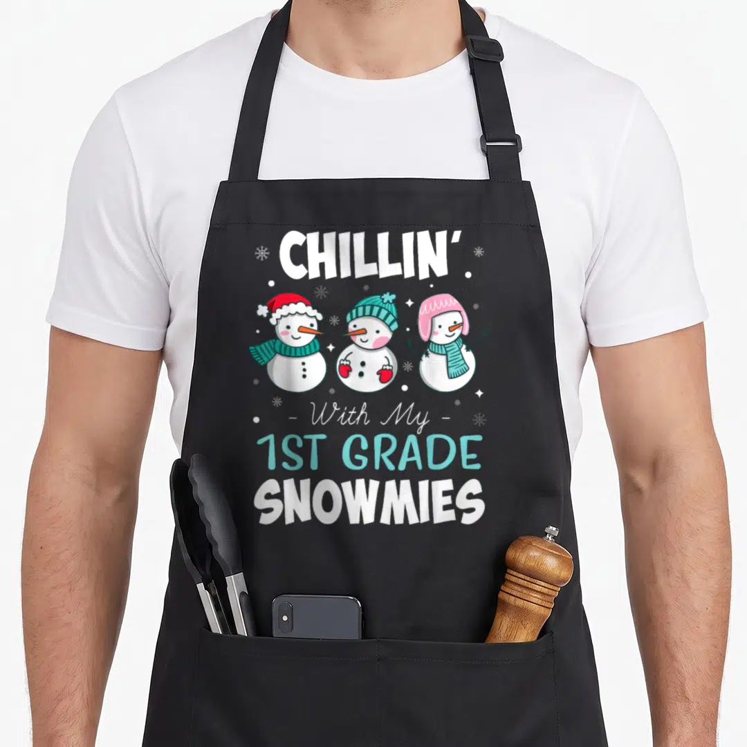 Chillin art teacher aprons - Three cartoon snowmen with hats and scarves under CHILLIN 1ST GRADE SNOWMIES text — shown on a black cotton canvas apron against a white background