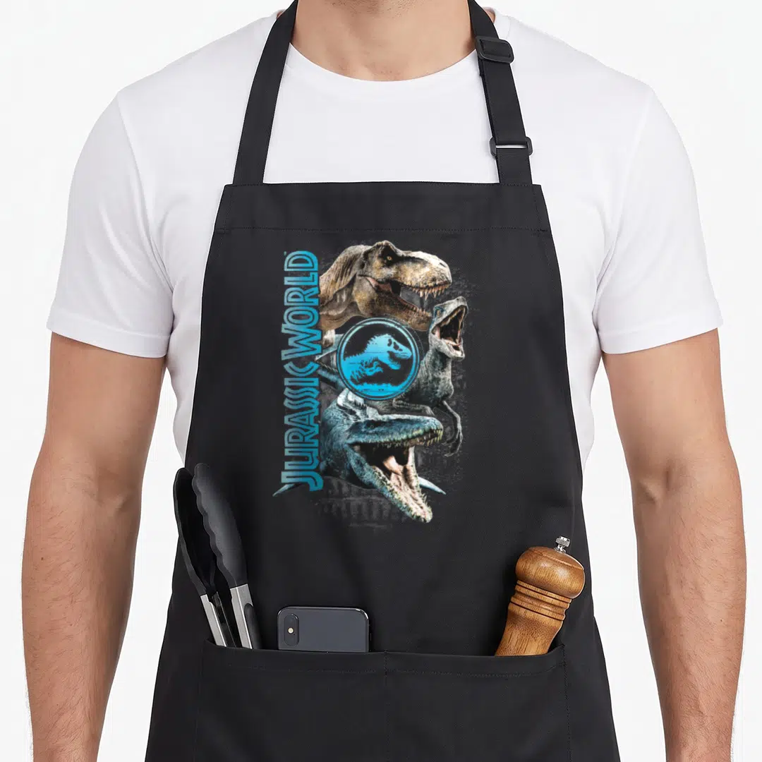 Stack dinosaur apron - Vertical JURASSIC WORLD text beside three stacked photo-style dinosaurs in blue, brown, and grey — shown on a black cotton canvas apron against a white background