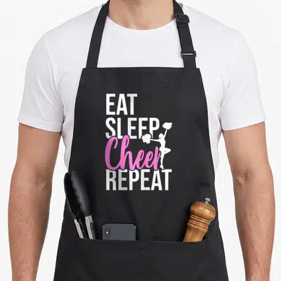 Eat gymnastics coach apron - Stacked EAT SLEEP Cheer REPEAT text with white cheerleader silhouette in pink and white — shown on a black cotton canvas apron against a white background