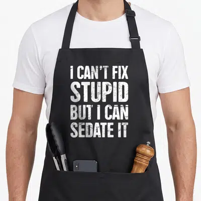 Sedate doctor apron - White distressed block text reading I CAN'T FIX STUPID BUT I CAN SEDATE IT stacked vertically — shown on a black cotton canvas apron against a white background