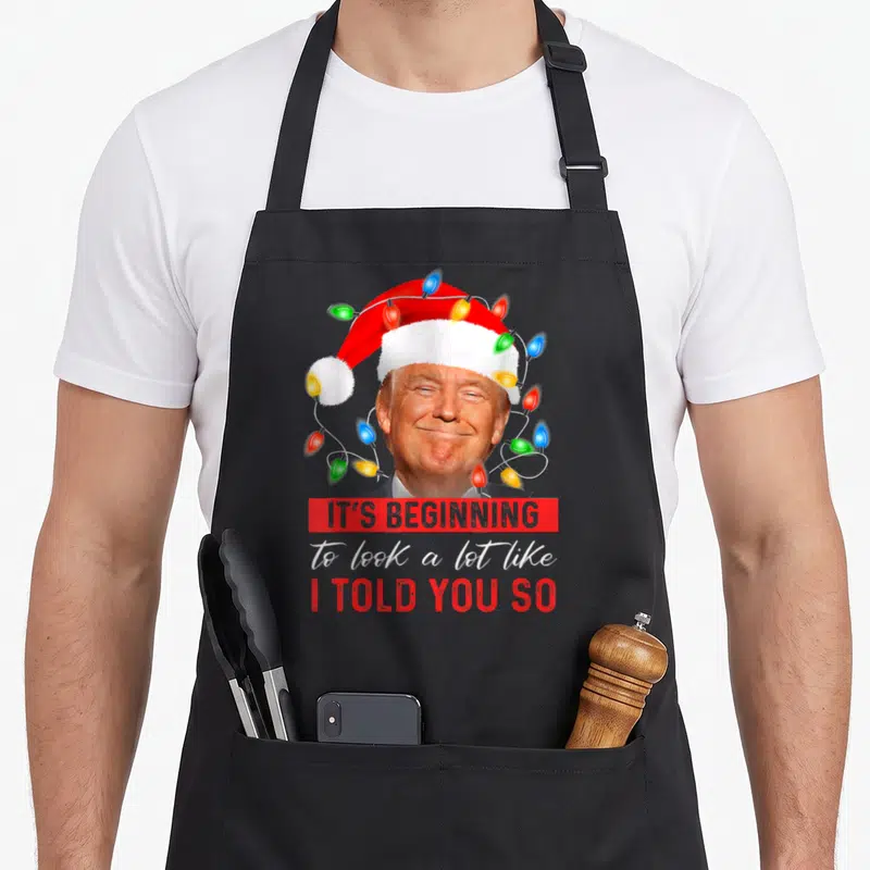 Beginning xmas apron - Donald Trump Santa hat lights IT'S BEGINNING I TOLD YOU SO text — shown on a black cotton canvas apron against a white background