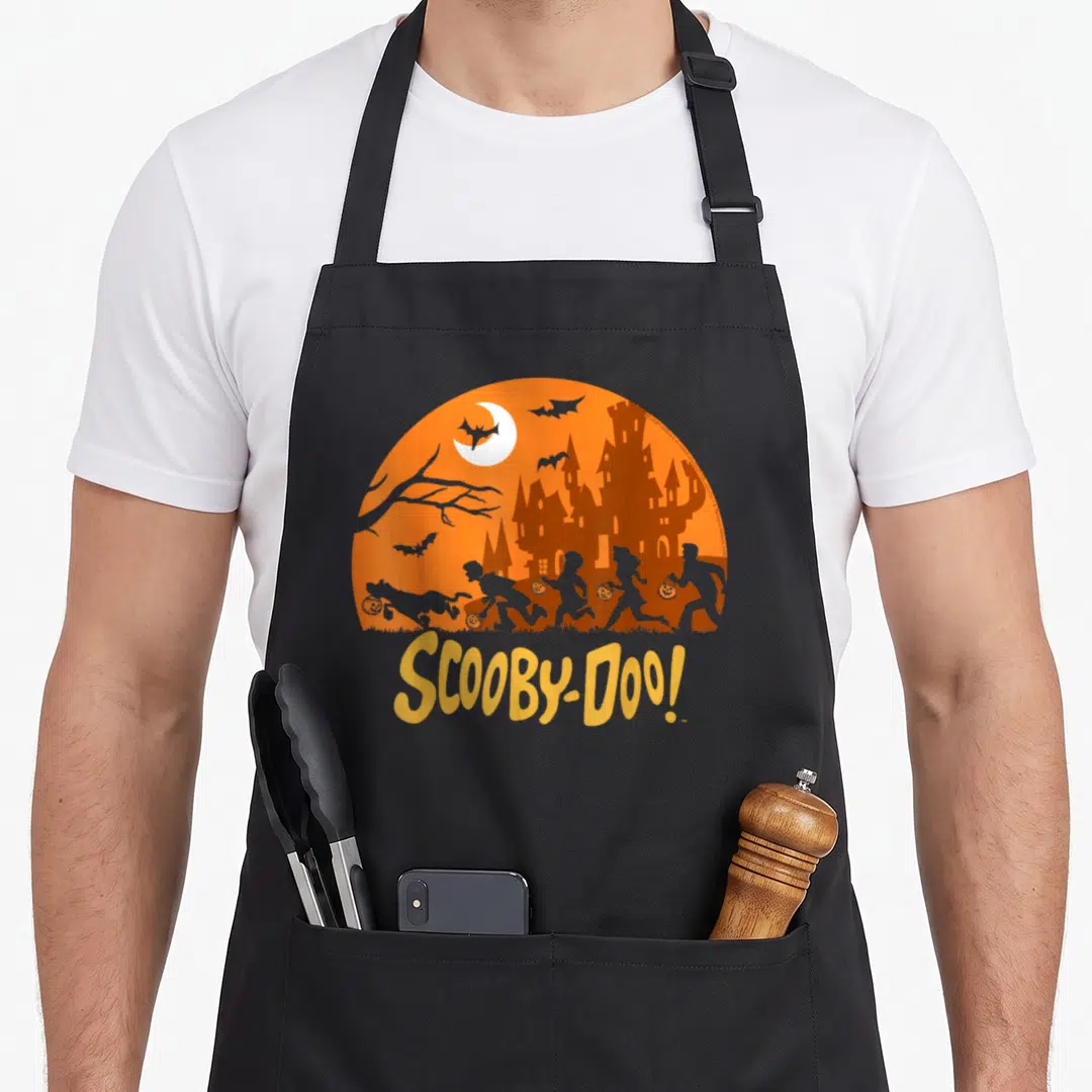 Gang halloween apron - Scooby-Doo gang silhouettes trick-or-treating near castle under orange moon with yellow logo text — shown on a black cotton canvas apron against a white background