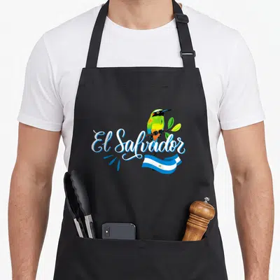 Solo salvadoran apron - Cartoon bird perched on branch with El Salvador script and waving flag in white blue green — shown on a black cotton canvas apron against a white background