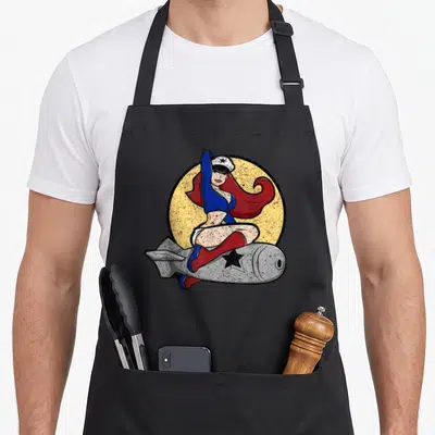 Ww2 pinup apron - Retro woman in blue top and red boots sitting on grey rocket with yellow circle background — shown on a black cotton canvas apron against a white background