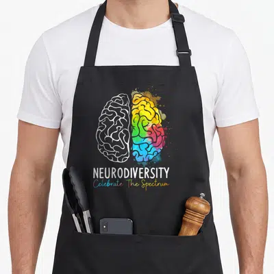 Neurodiversity rainbow apron - Split brain graphic with white outline and colorful watercolor splashes below — shown on a black cotton canvas apron against a white background