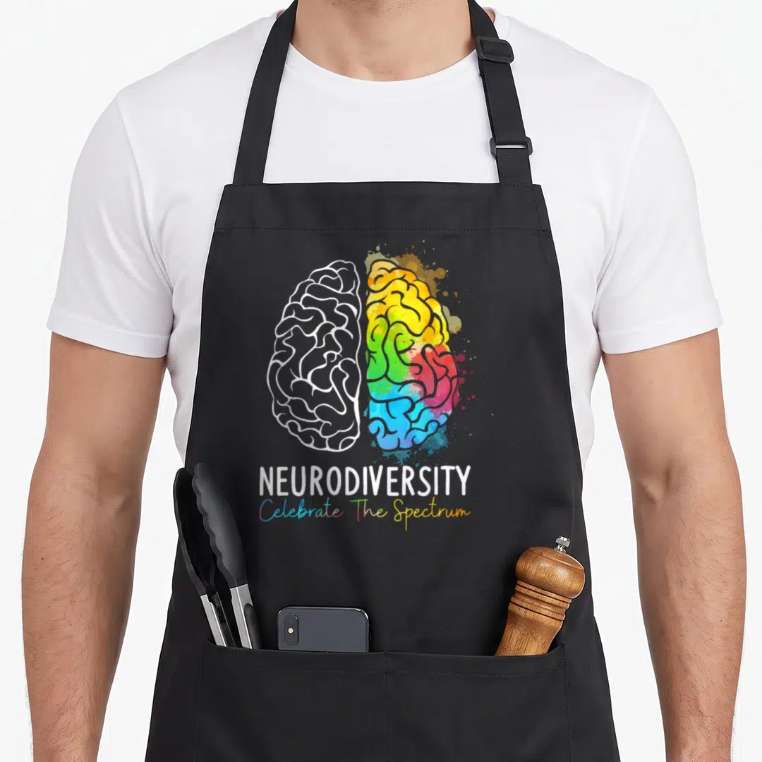 Neurodiversity rainbow apron - Split brain graphic with white outline and colorful watercolor splashes below — shown on a black cotton canvas apron against a white background
