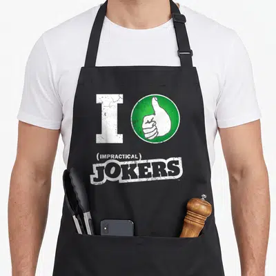 Thumb fools apron - White I and green thumbs-up circle above (IMPRACTICAL) JOKERS distressed text — shown on a black cotton canvas apron against a white background