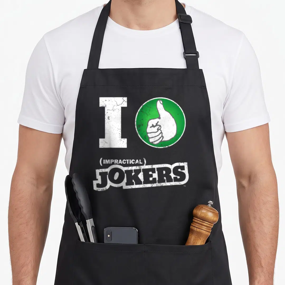 Thumb fools apron - White I and green thumbs-up circle above (IMPRACTICAL) JOKERS distressed text — shown on a black cotton canvas apron against a white background