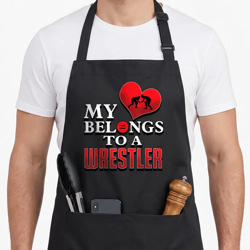 Wrestling grandma apron - Red heart with two black wrestlers above My Belongs to a Wrestler text — shown on a black cotton canvas apron against a white background