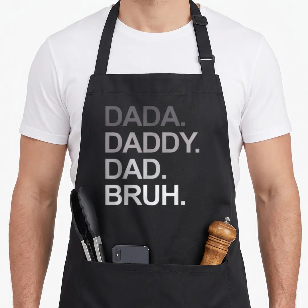 Bruh father day apron - Stacked grey text DADA DADDY DAD BRUH on black background — shown on a black cotton canvas apron against a white background