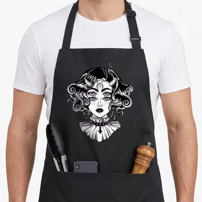 Horned goth apron - Black and white line art of a four-eyed horned woman with an inverted cross and floating diamonds — shown on a black cotton canvas apron against a white background