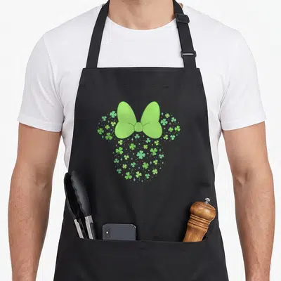 Icon st patrick day aprons - Green bow above circular cluster of shamrocks and stars — shown on a black cotton canvas apron against a white background
