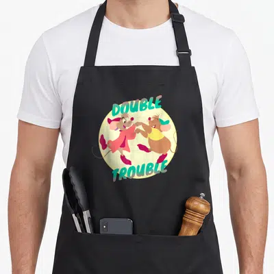 Cinderella double apron - Two cartoon mice holding paws in a yellow circle under arched teal text reading DOUBLE TROUBLE — shown on a black cotton canvas apron against a white background