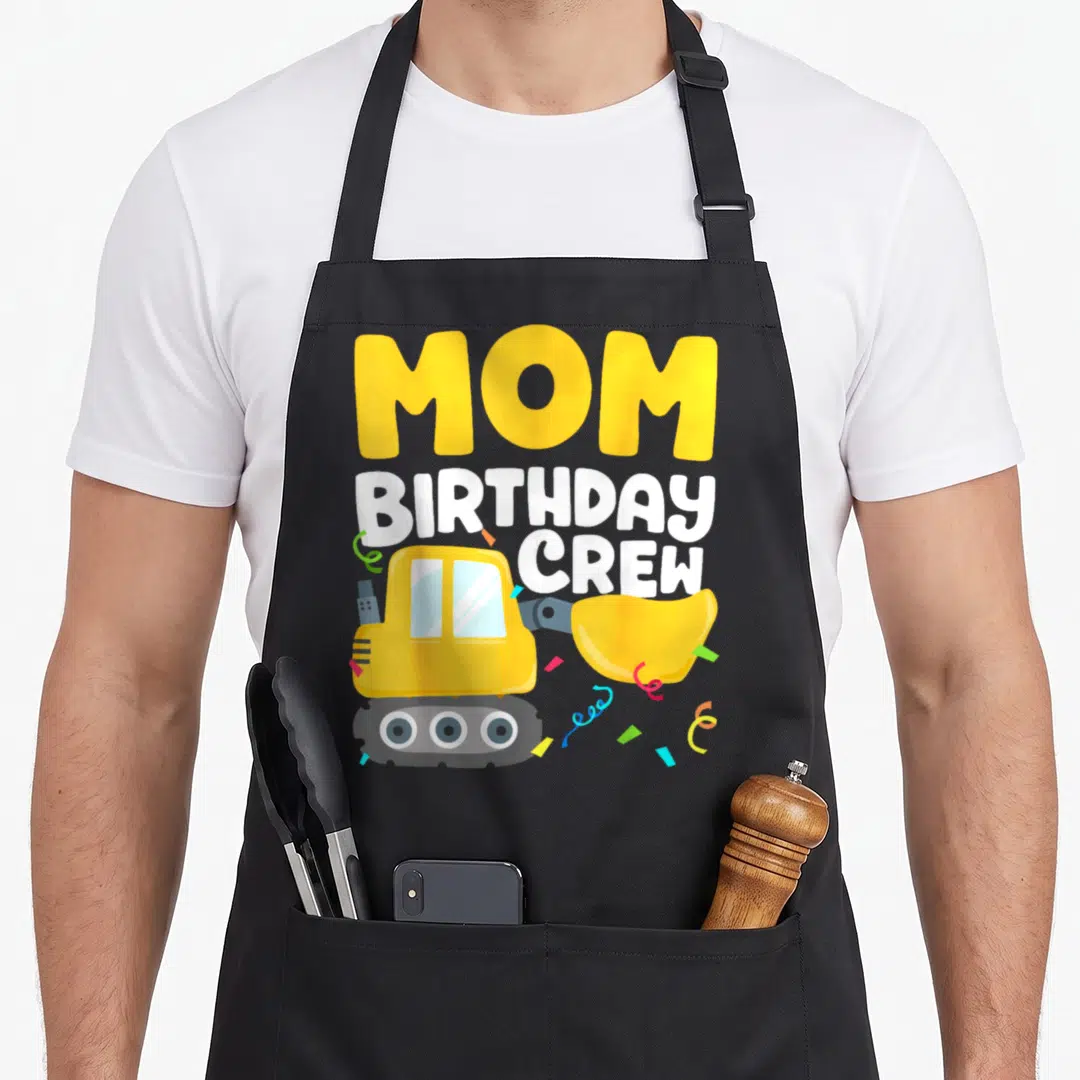 Truck crew aprons - MOM BIRTHDAY CREW text above yellow excavator and colorful confetti — shown on a black cotton canvas apron against a white background