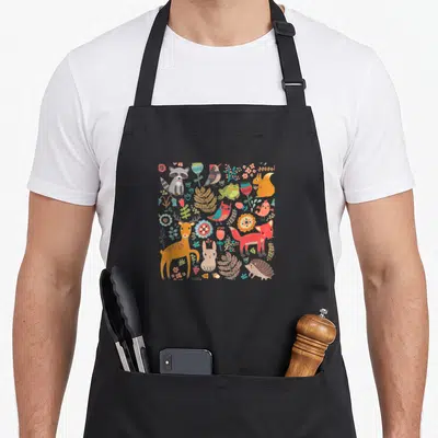 Nature animal apron - Cartoon forest animals and plants in a square arrangement with orange, green, and red details — shown on a black cotton canvas apron against a white background