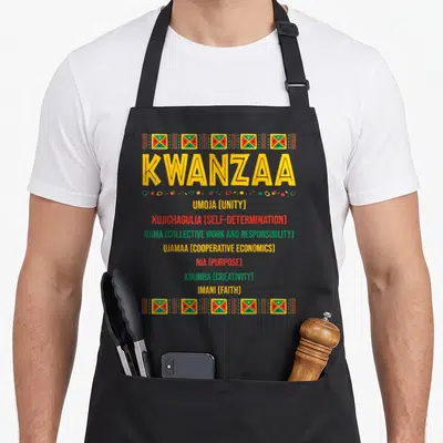 Christmas african american aprons - Kwanzaa text listing seven principles between yellow red green and black geometric — shown on a black cotton canvas apron against a white background