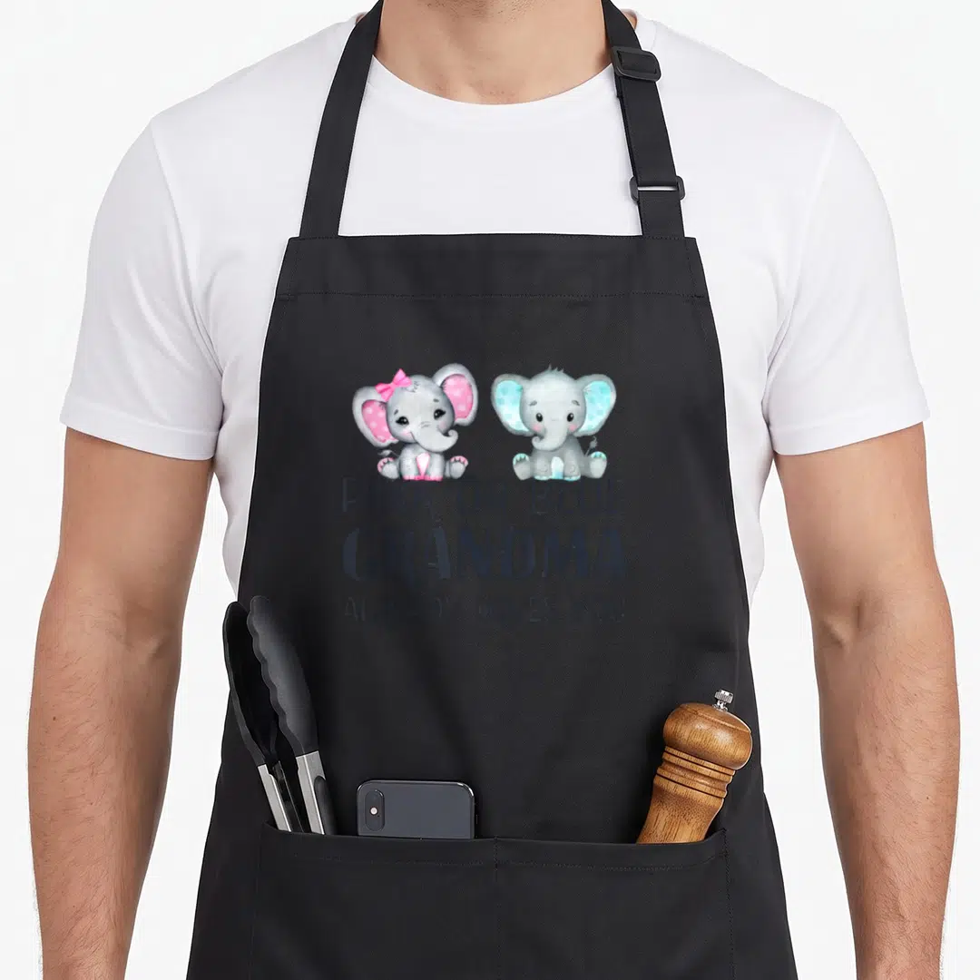 Already grandma apron - Two grey elephants with pink and blue accents above PINK OR BLUE GRANDMA ALREADY LOVES YOU text — shown on a black cotton canvas apron against a white background