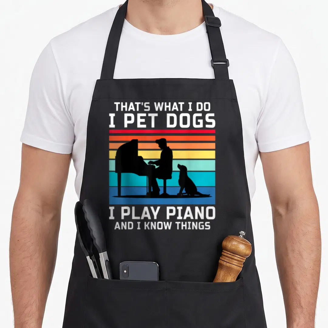 Pet piano apron - Text reading I Play Piano next to black silhouette of man and dog on colored stripes — shown on a black cotton canvas apron against a white background