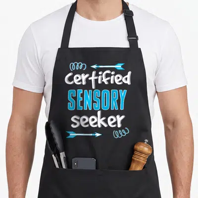 Spd sensory apron - Stacked text Certified SENSORY seeker with blue arrows and scribbles in white and blue — shown on a black cotton canvas apron against a white background