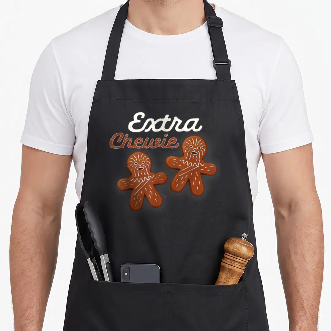 Extra gingerbread apron - Two brown gingerbread men with white icing fur details and Extra Chewie text — shown on a black cotton canvas apron against a white background