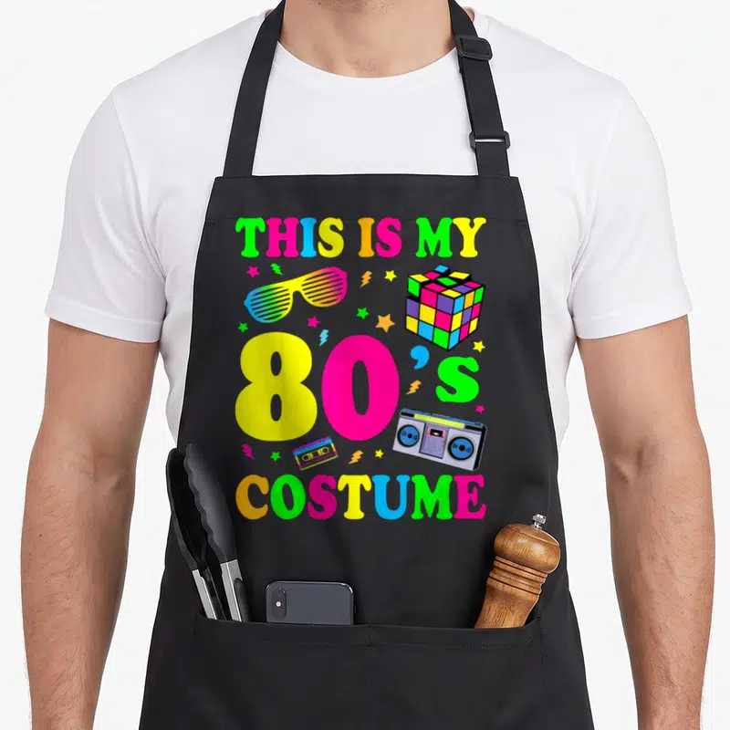 Costume 90s 80s apron - Neon text reading THIS IS MY 80S COSTUME with boombox, cassette, rubiks cube, sunglasses, stars — shown on a black cotton canvas apron against a white background