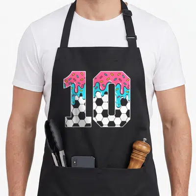 Soccer ice cream apron - Number 10 with pink blue drip frosting yellow sprinkles and grey white soccer ball pattern — shown on a black cotton canvas apron against a white background
