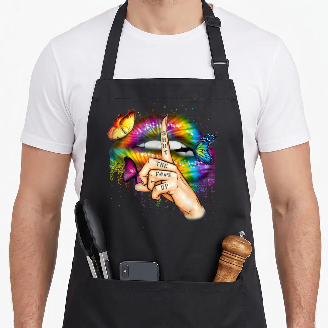 Trippy tie-dye apron - Hand with SHUT THE F@#% UP tattoo in front of rainbow lips and three butterflies — shown on a black cotton canvas apron against a white background