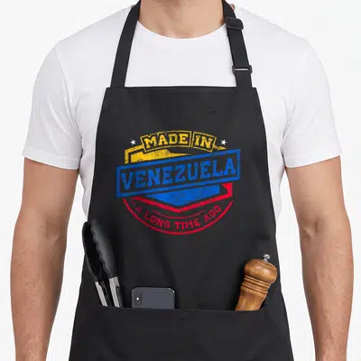 Venezuela aboriginal apron - Yellow blue and red stamp reading Made In Venezuela A Long Time Ago with two white stars — shown on a black cotton canvas apron against a white background