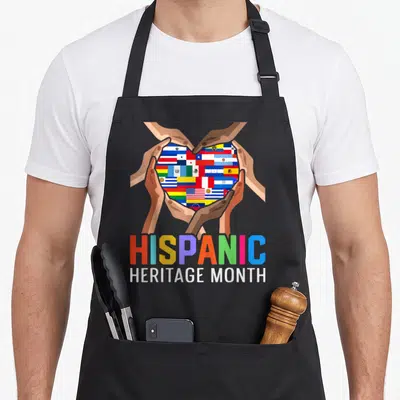 Latin country apron - Four hands holding heart of flags with Hispanic Heritage Month text — shown on a black cotton canvas apron against a white background