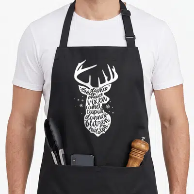 Holiday reindeer christmas apron - White deer silhouette containing stacked names of nine reindeer including Rudolph — shown on a black cotton canvas apron against a white background