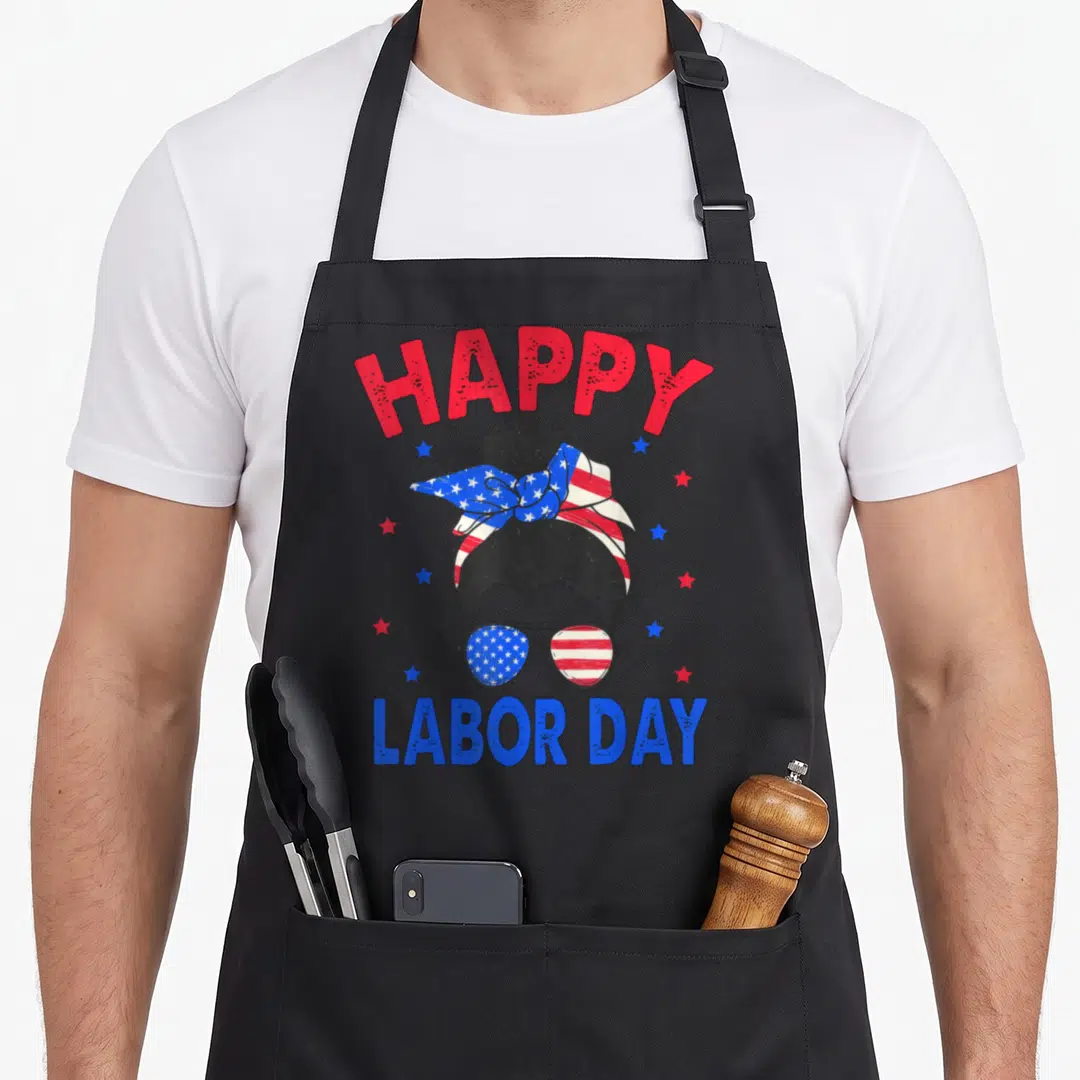 Labor bun messy aprons - Woman with flag headband and sunglasses under arched HAPPY LABOR DAY text with scattered stars — shown on a black cotton canvas apron against a white background