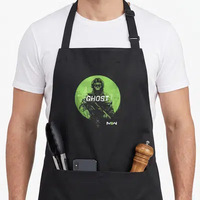 Ghost video game apron - Stacked GHOST text over skull soldier silhouette in green circle with geometric lines — shown on a black cotton canvas apron against a white background