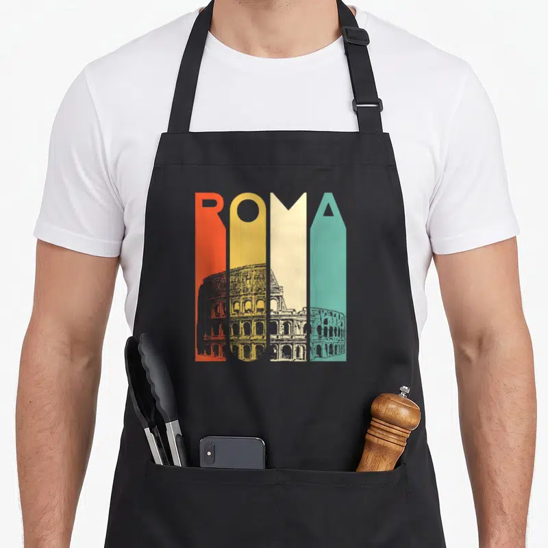Roma italian apron - Colorful ROMA text with grey Colosseum sketch overlay across bottom half of letters — shown on a black cotton canvas apron against a white background