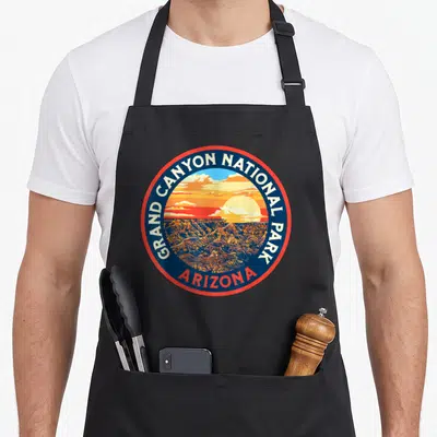 Park 80s apron - Circular Grand Canyon National Park emblem with sunset landscape and Arizona text — shown on a black cotton canvas apron against a white background