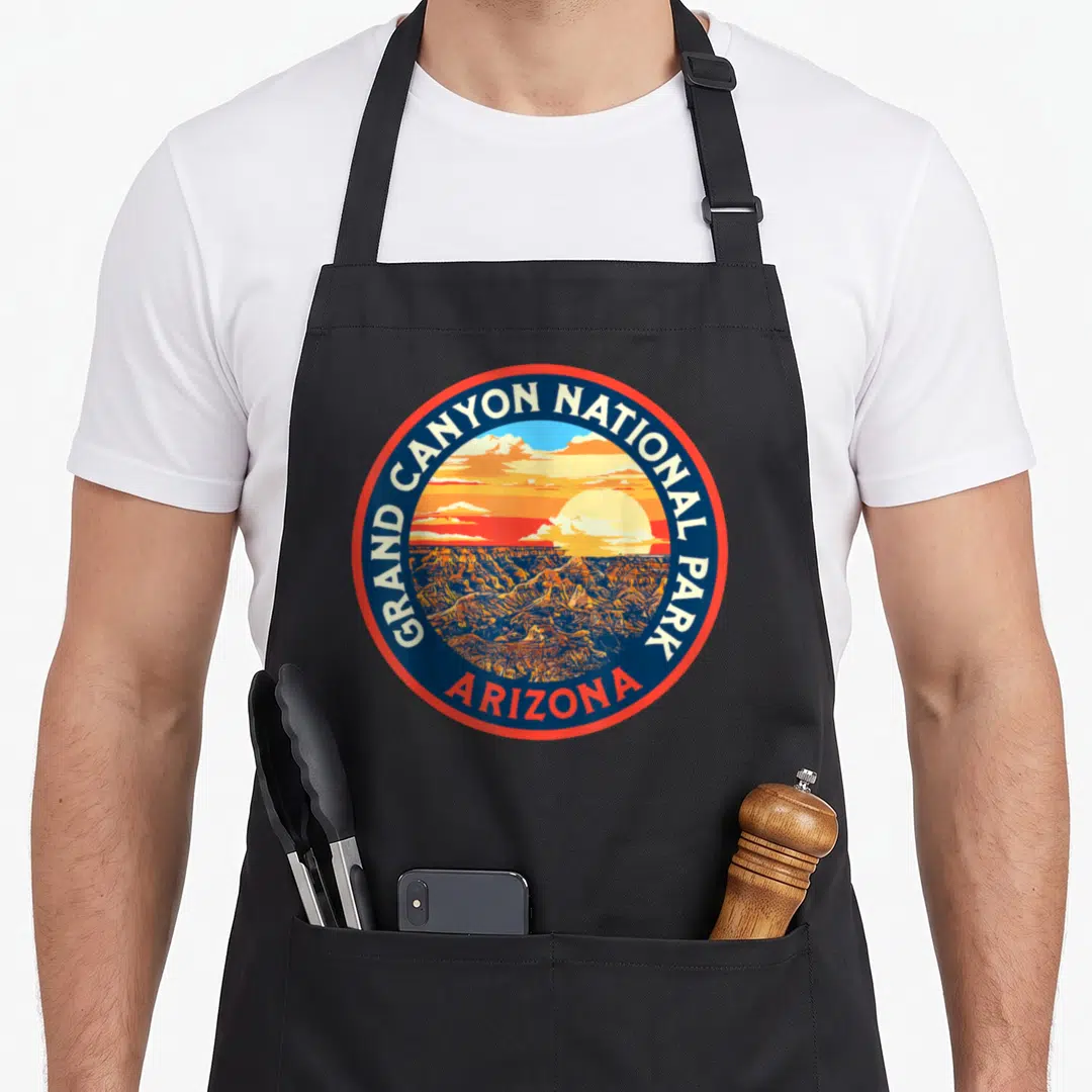 Park 80s apron - Circular Grand Canyon National Park emblem with sunset landscape and Arizona text — shown on a black cotton canvas apron against a white background