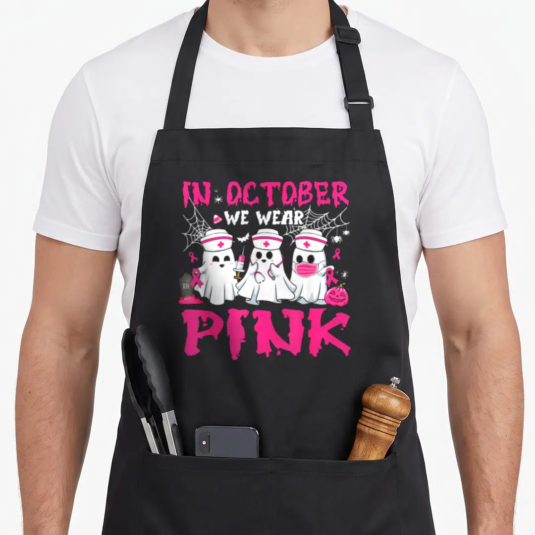 October halloween nurse apron - Three ghost nurses holding pink ribbons and syringes surrounded by spider webs — shown on a black cotton canvas apron against a white background