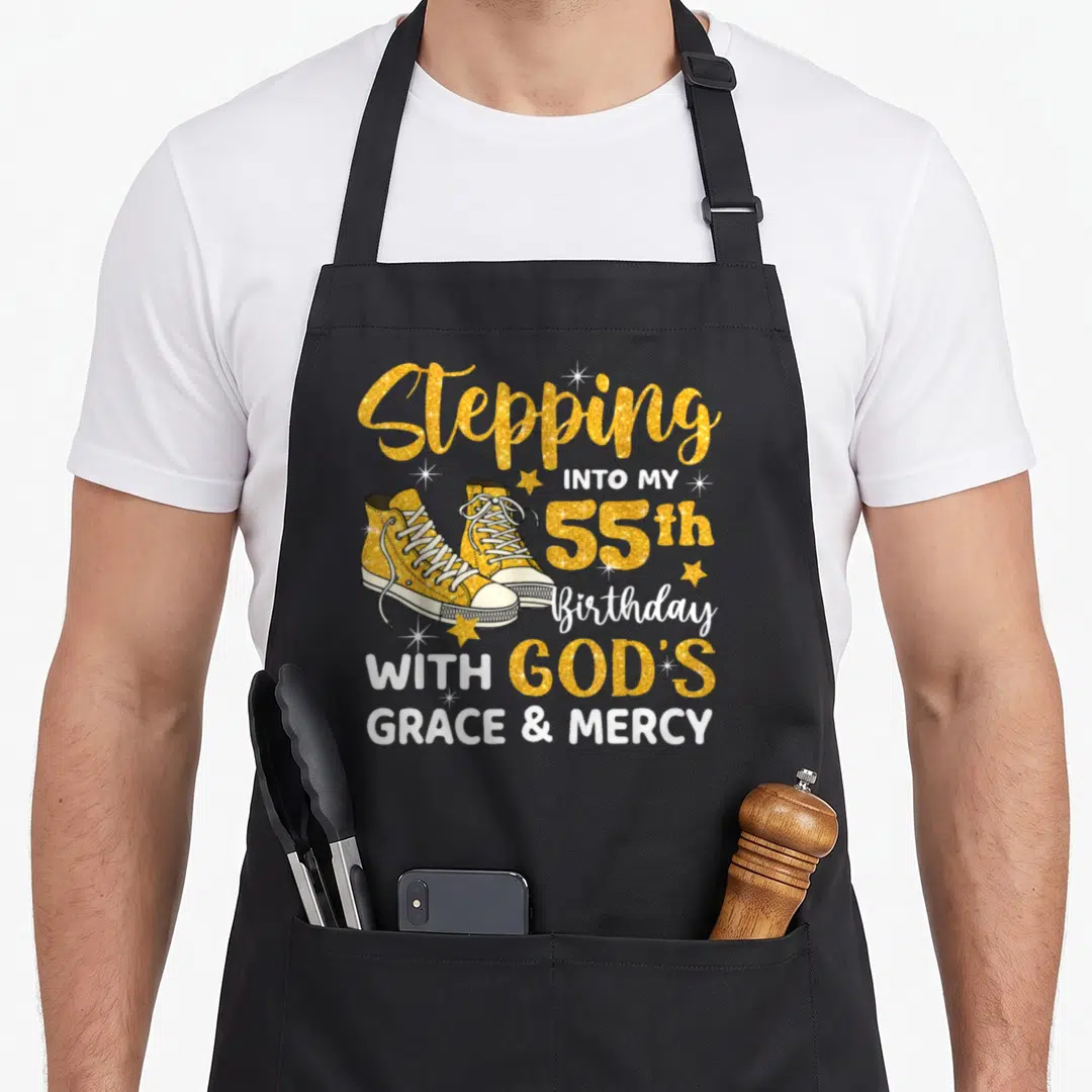 Grace birthday apron - Gold sneakers and text Stepping Into My 55th Birthday With God's Grace Mercy — shown on a black cotton canvas apron against a white background
