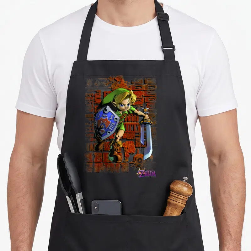Mask legend apron - Link holding shield and sword with green tunic against distressed orange background and purple logo — shown on a black cotton canvas apron against a white background