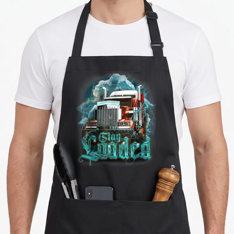 Truckin semi truck apron - Orange semi-truck with cyan lightning and clouds, text reads Gay Loaded in gothic font — shown on a black cotton canvas apron against a white background