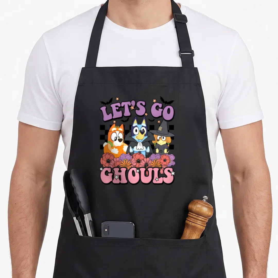 Blue heeler halloween apron - Three cartoon dogs in Halloween costumes below Let's Go Ghouls text and above pink — shown on a black cotton canvas apron against a white background
