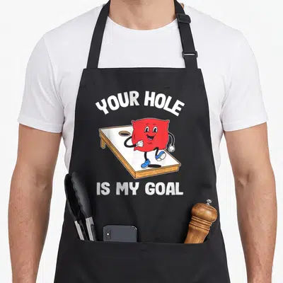 Hole sarcastic apron - Red cartoon bean bag on board with YOUR HOLE IS MY GOAL text — shown on a black cotton canvas apron against a white background