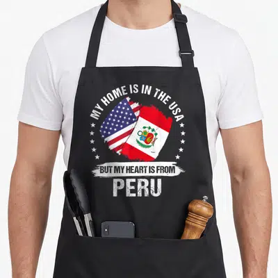 Peru patriots apron - My Home Is In The USA But My Heart Is From Peru text with overlapping US and Peru flags — shown on a black cotton canvas apron against a white background