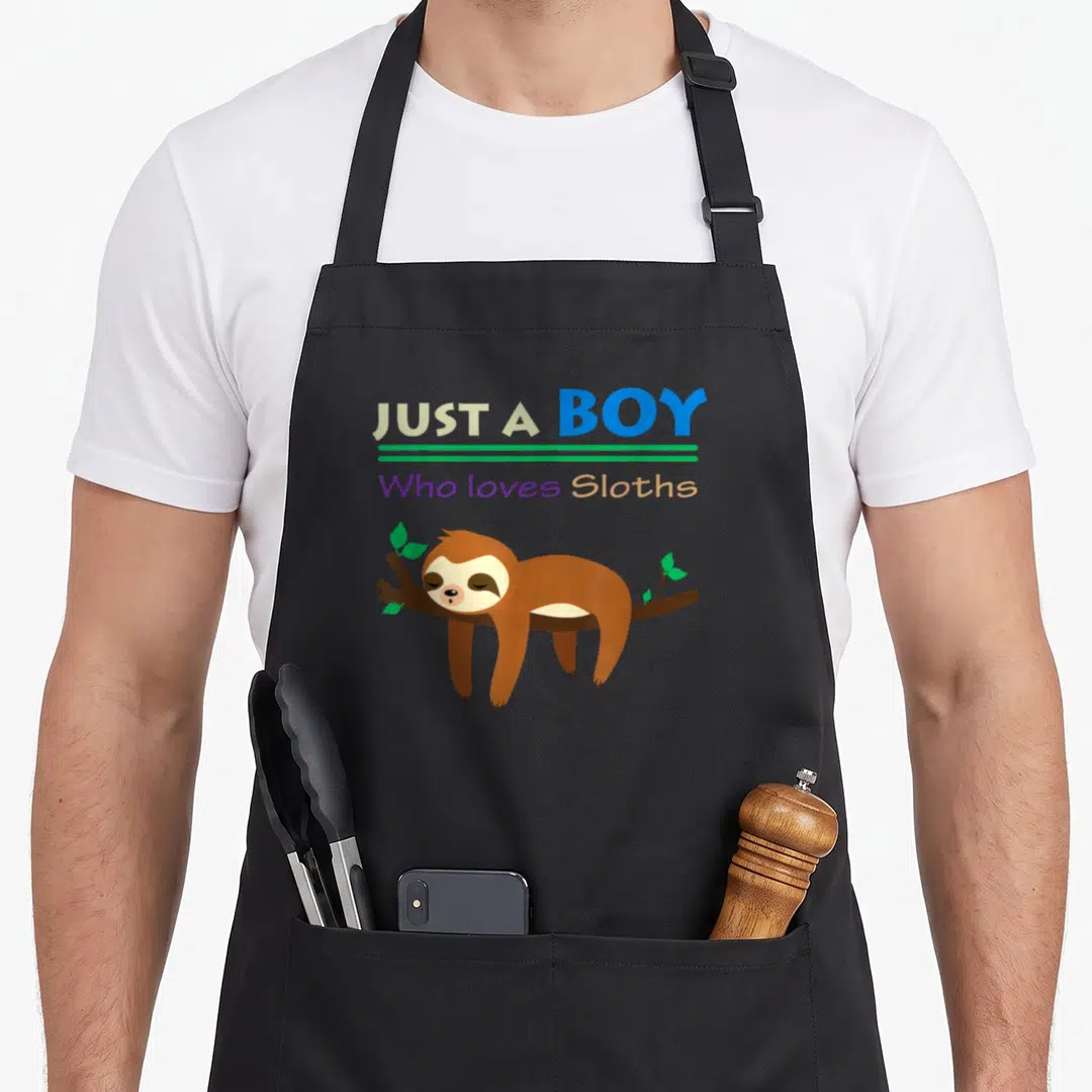 Funny lazy sloth apron - Text Just A Boy Who loves Sloths above cartoon sloth lying on branch — shown on a black cotton canvas apron against a white background