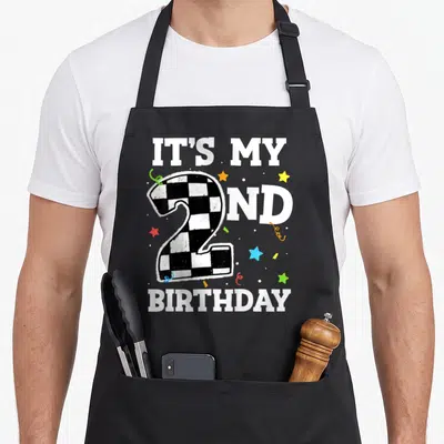 Racing car 2nd apron - Checkered number 2 with IT'S MY ND BIRTHDAY text and colorful stars — shown on a black cotton canvas apron against a white background