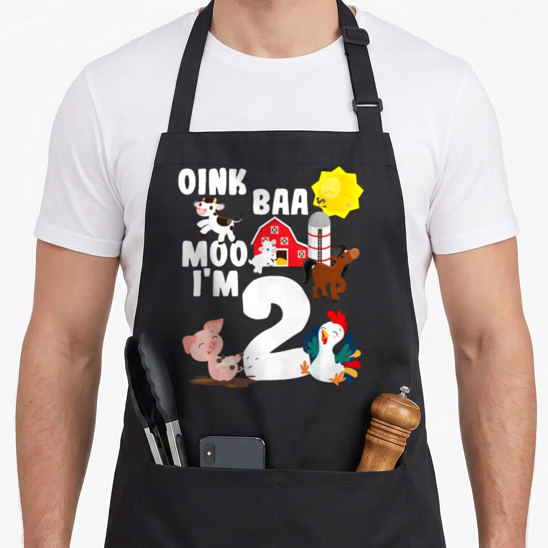 Baa farm aprons - Cartoon cow pig sheep horse rooster barn sun around white number 2 text Oink Baa Moo I'm 2 — shown on a black cotton canvas apron against a white background