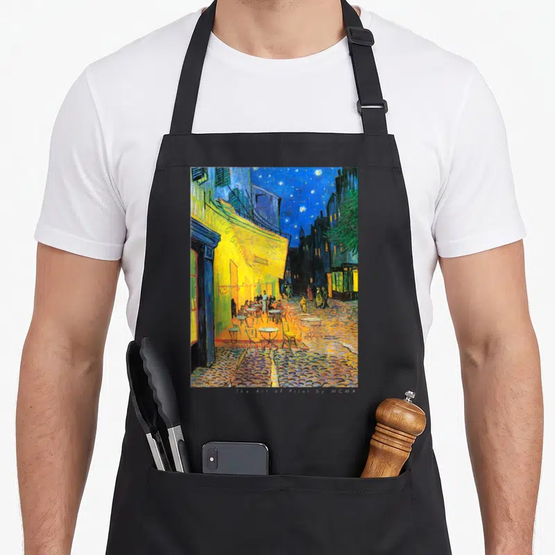 Cafe van gogh apron - Reproduction of the street cafe terrace at night painting in yellow and blue on black fabric — shown on a black cotton canvas apron against a white background