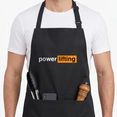 Gym powerlifting addict apron - White power text next to black lifting text inside an orange rectangle — shown on a black cotton canvas apron against a white background