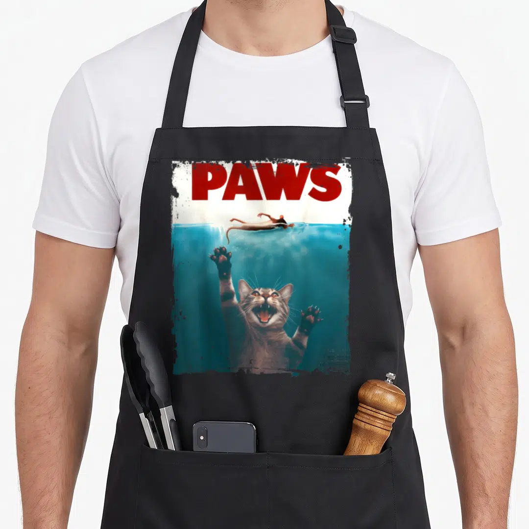 Paw meow kitten apron - Red PAWS text above a grey cat underwater reaching for a floating mouse — shown on a black cotton canvas apron against a white background