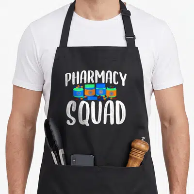 Squad pharmacist apron - PHARMACY SQUAD text above blue green orange pill bottles and scattered pills — shown on a black cotton canvas apron against a white background